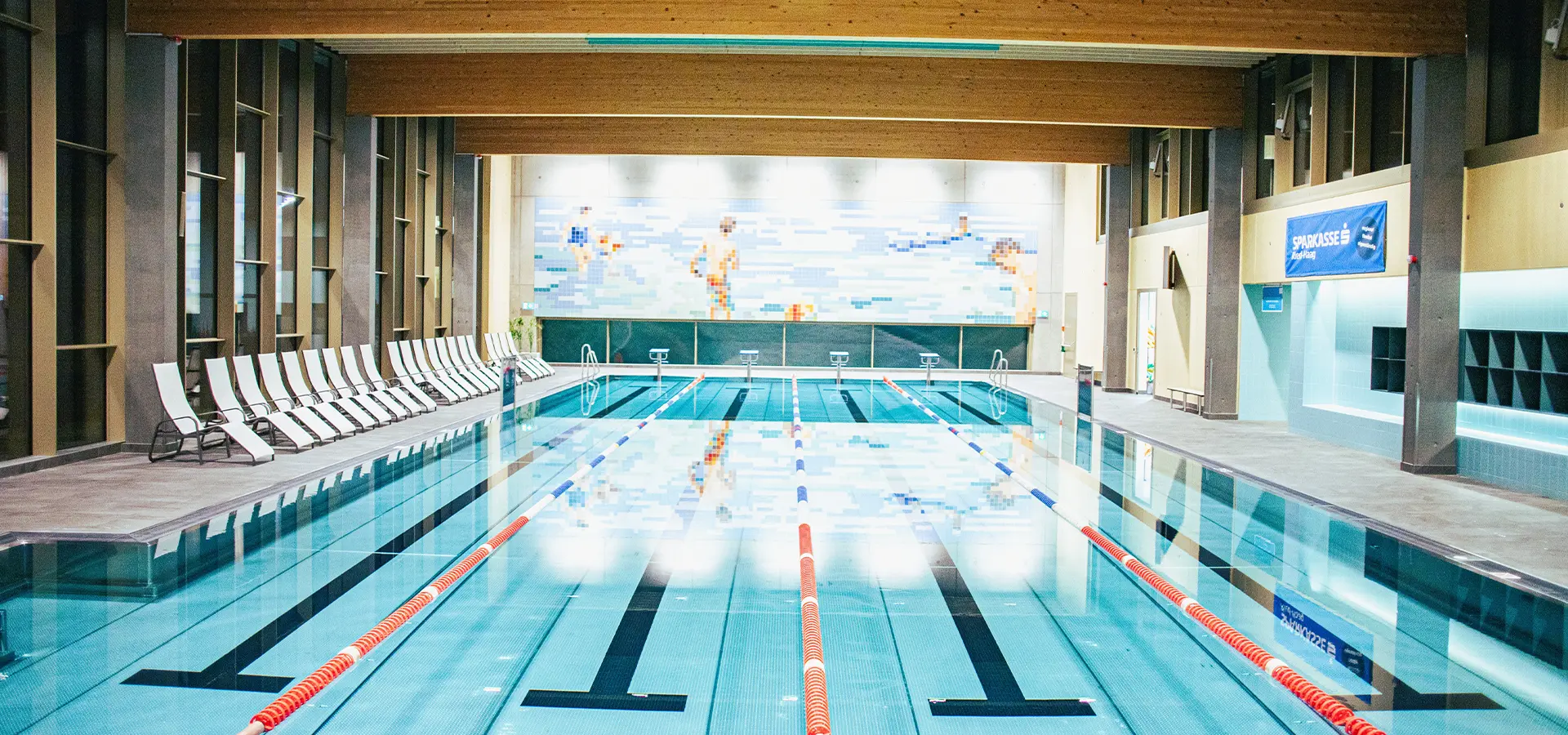 Blick auf das 25 Meter Sportbecken am Abend. Das Wandbild spiegelt sich im Wasser
