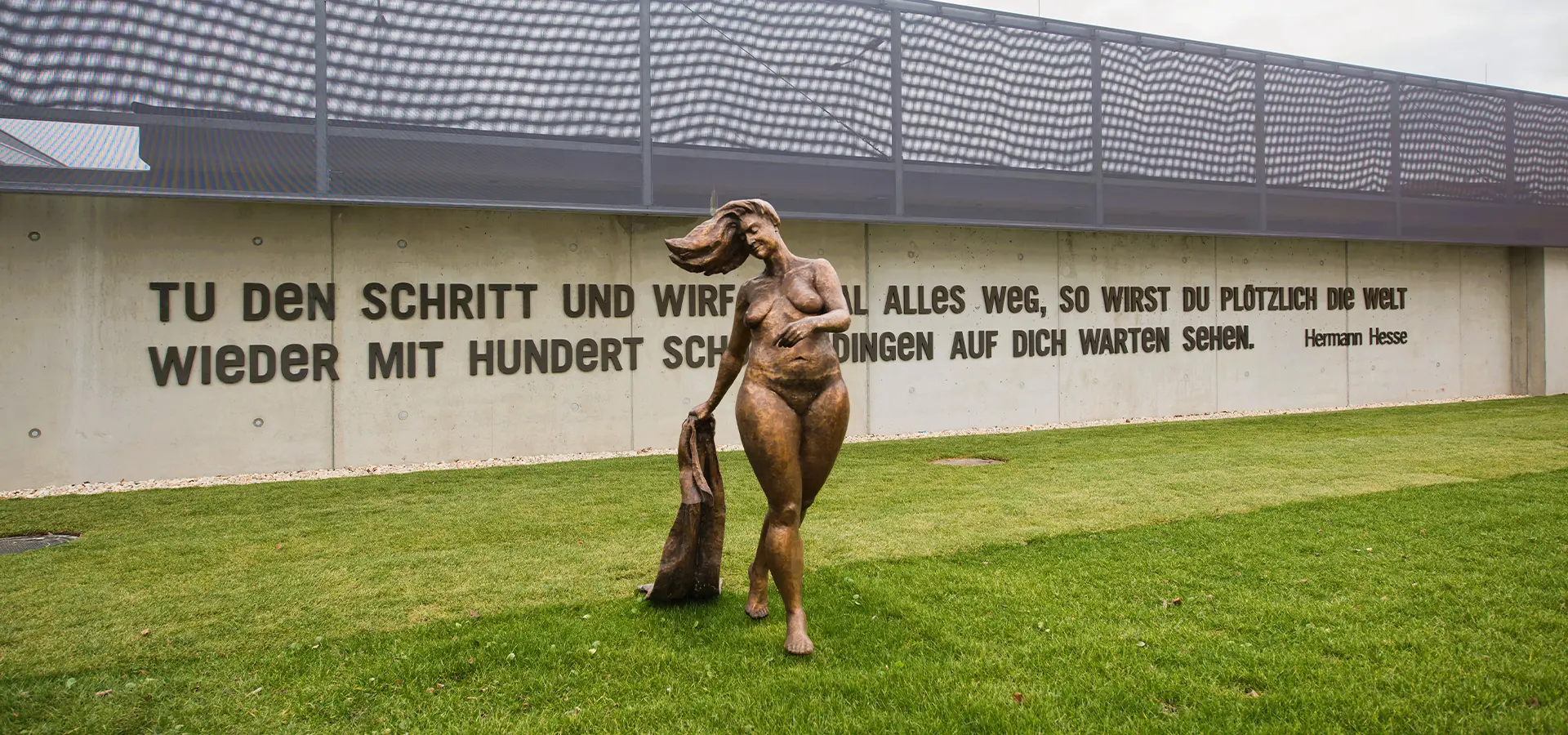 Außenfoto einer Bronzestatur von einer nackten Frau mit Handtuch.