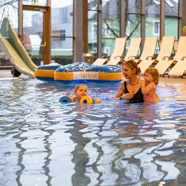 Mama spielt mit ihren 2 Kindern im Familienbecken