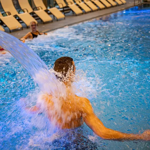 Ein Mann steht unter der laufenden Schwalldusche und lässt sich massieren.