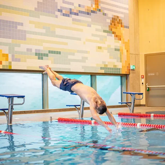 Mann Springt beim 25 Meter Sportbecken mit einem Kopfsprung vom Startsockel