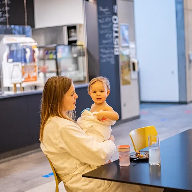 Frau mit Kleinkind am Tisch und im Hintergrund die Theke