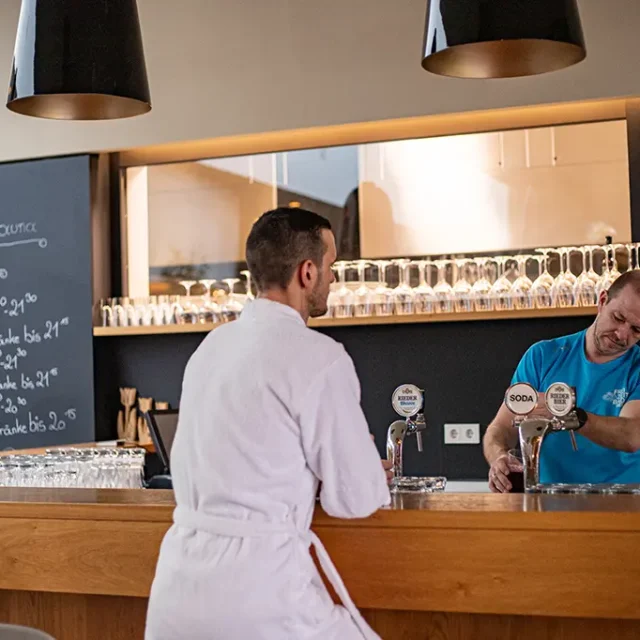 Mitarbeiter schenkt einem Gast in Bademantel ein Getränk ein