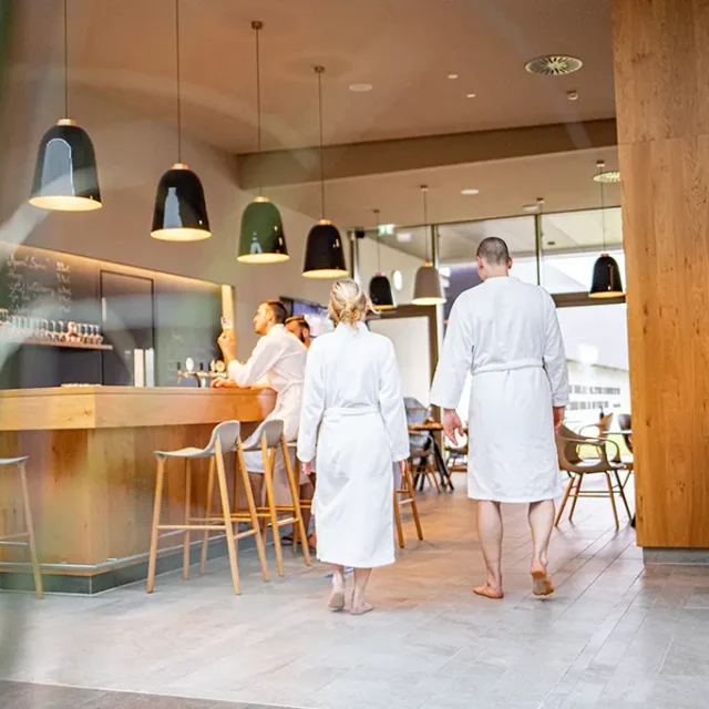 Badegäste mit Bademänteln in der Saunalounge mit Bar und Sitzmöglichkeiten