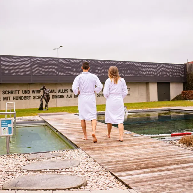 Zwei Badegäste in Bademantel gehen über Wassersteg