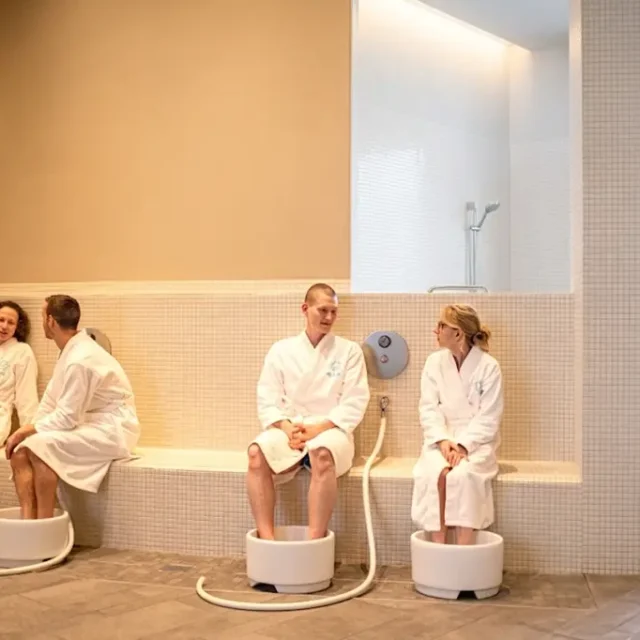 Badegäste in Bademänteln sitzen mit den Füßen im Fußbad und unterhalten sich