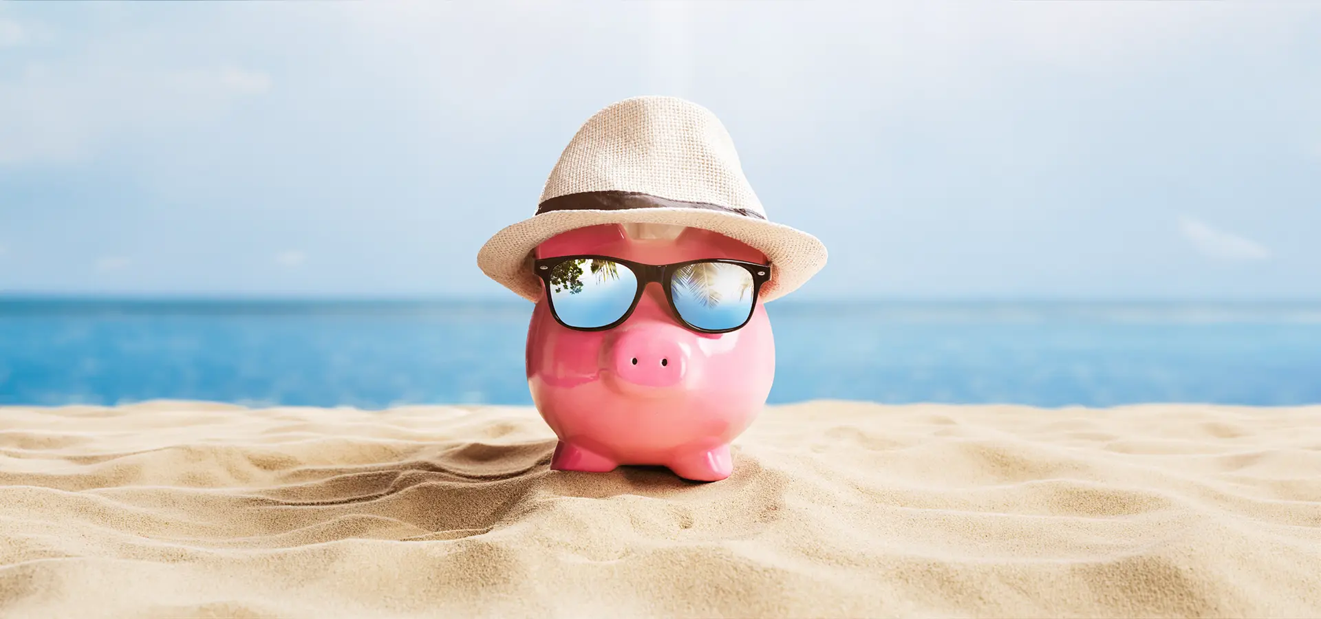Sparschwein mit Sonnenbrille und Hut am Strand