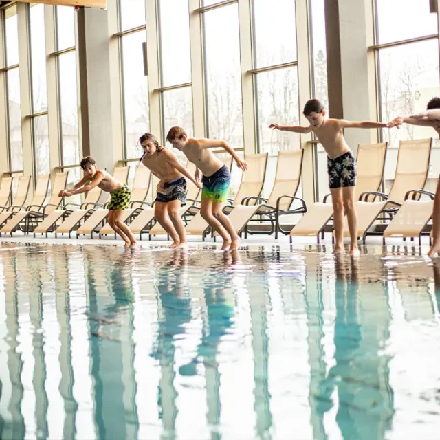 Gruppe von Kindern in Badehosen springen vom Beckenrand ins Wasser
